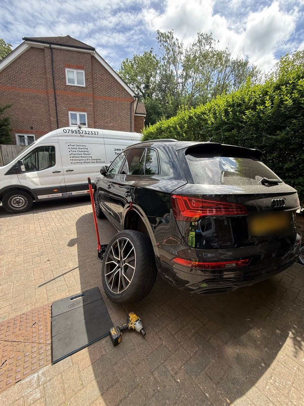 A black Audi Q5 with its rear wheel off on a trolley jack, an impact gun on the ground and a JL Mobile Tyres van behind