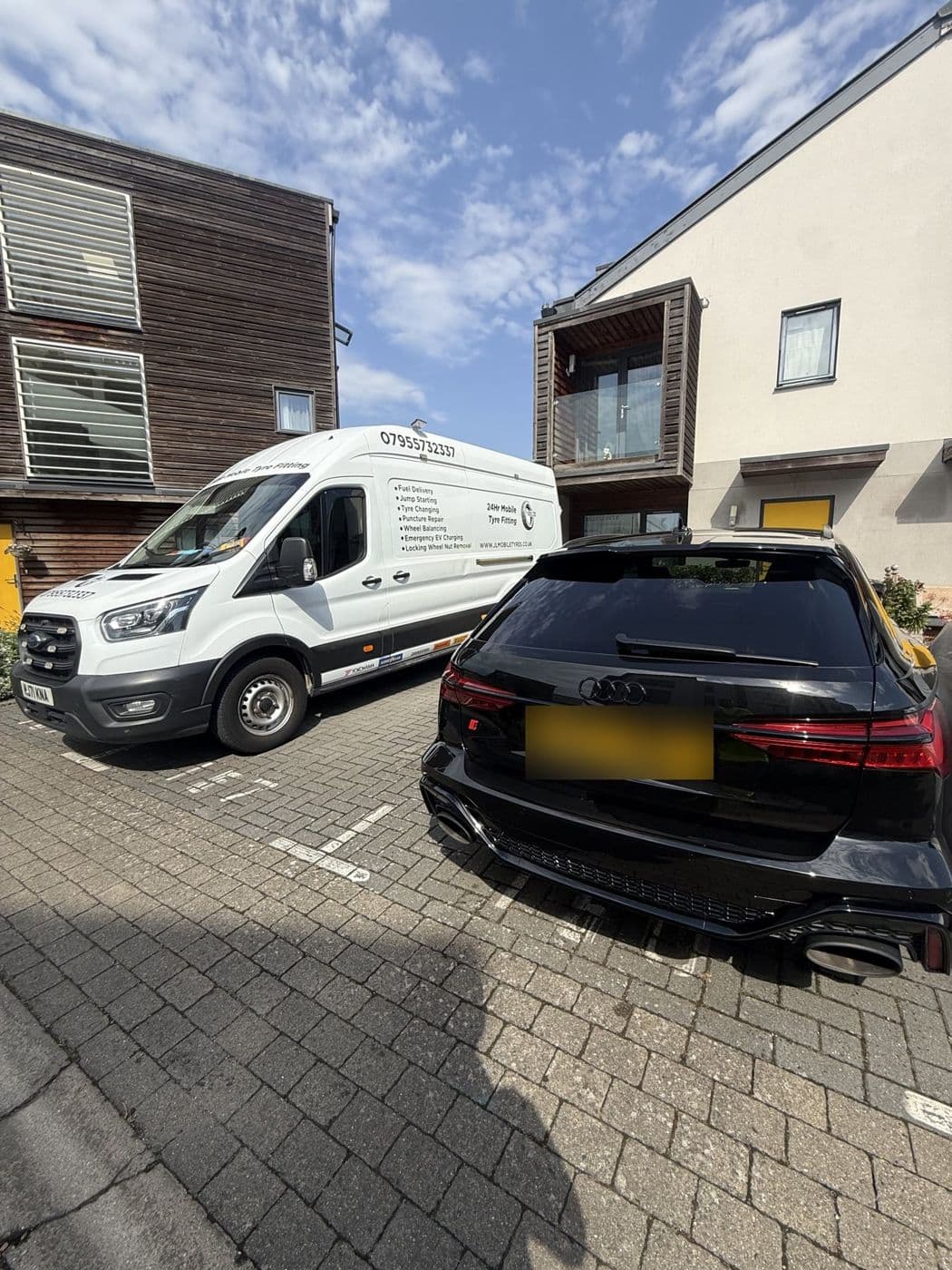 A black Audi estate parked on block paving beside a JL Mobile Tyres van