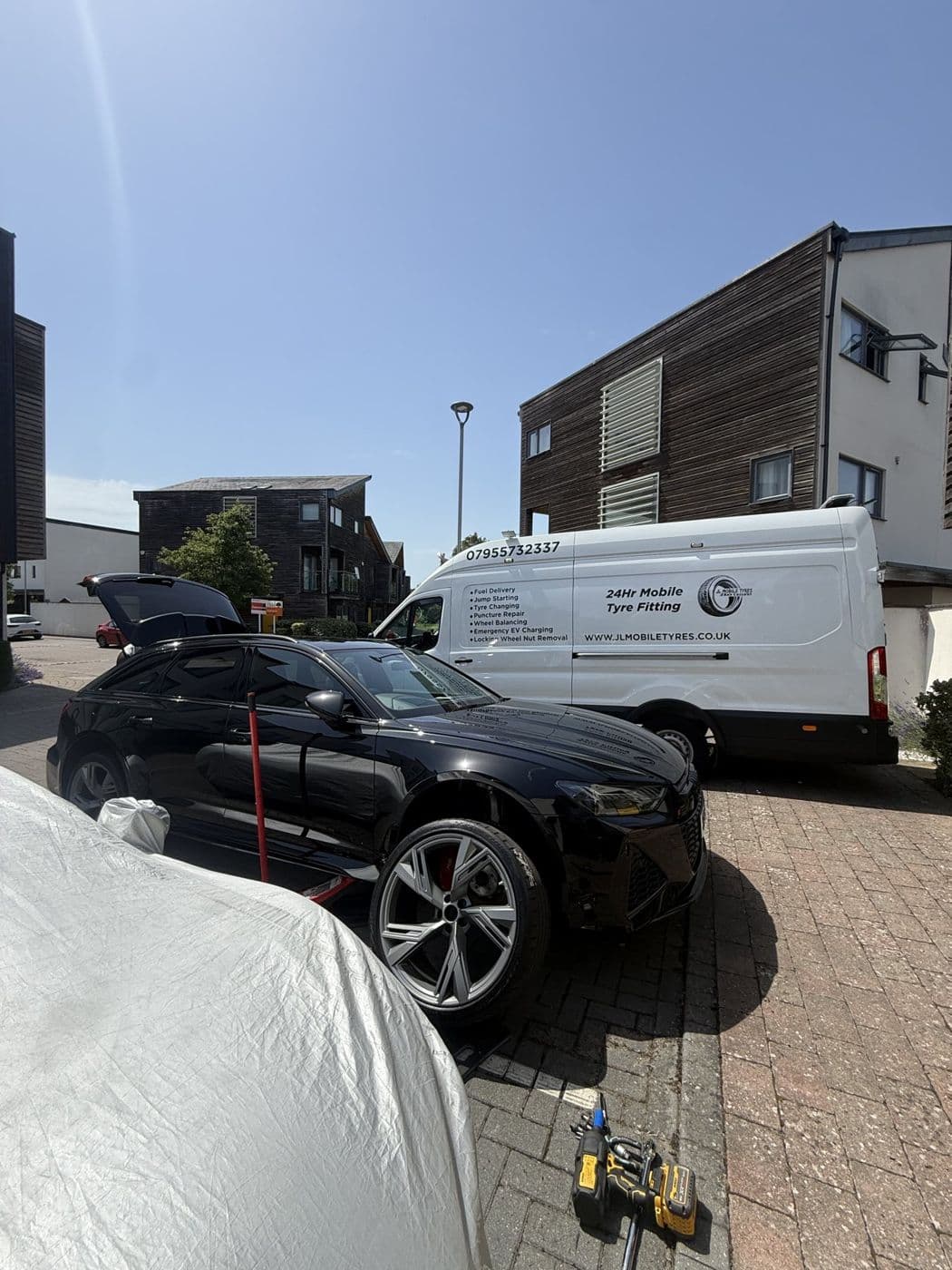A black Audi on a driveway with one wheel off and a JL Mobile Tyres van parked behind