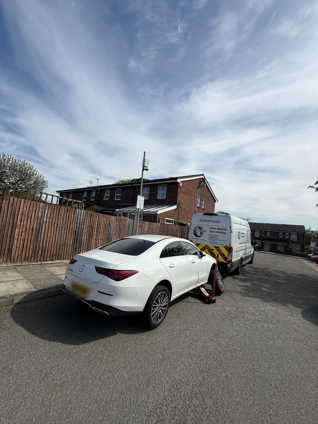 A white Mercedes on a trolley jack at the kerb of a residential street, a JL Mobile Tyres van parked in front