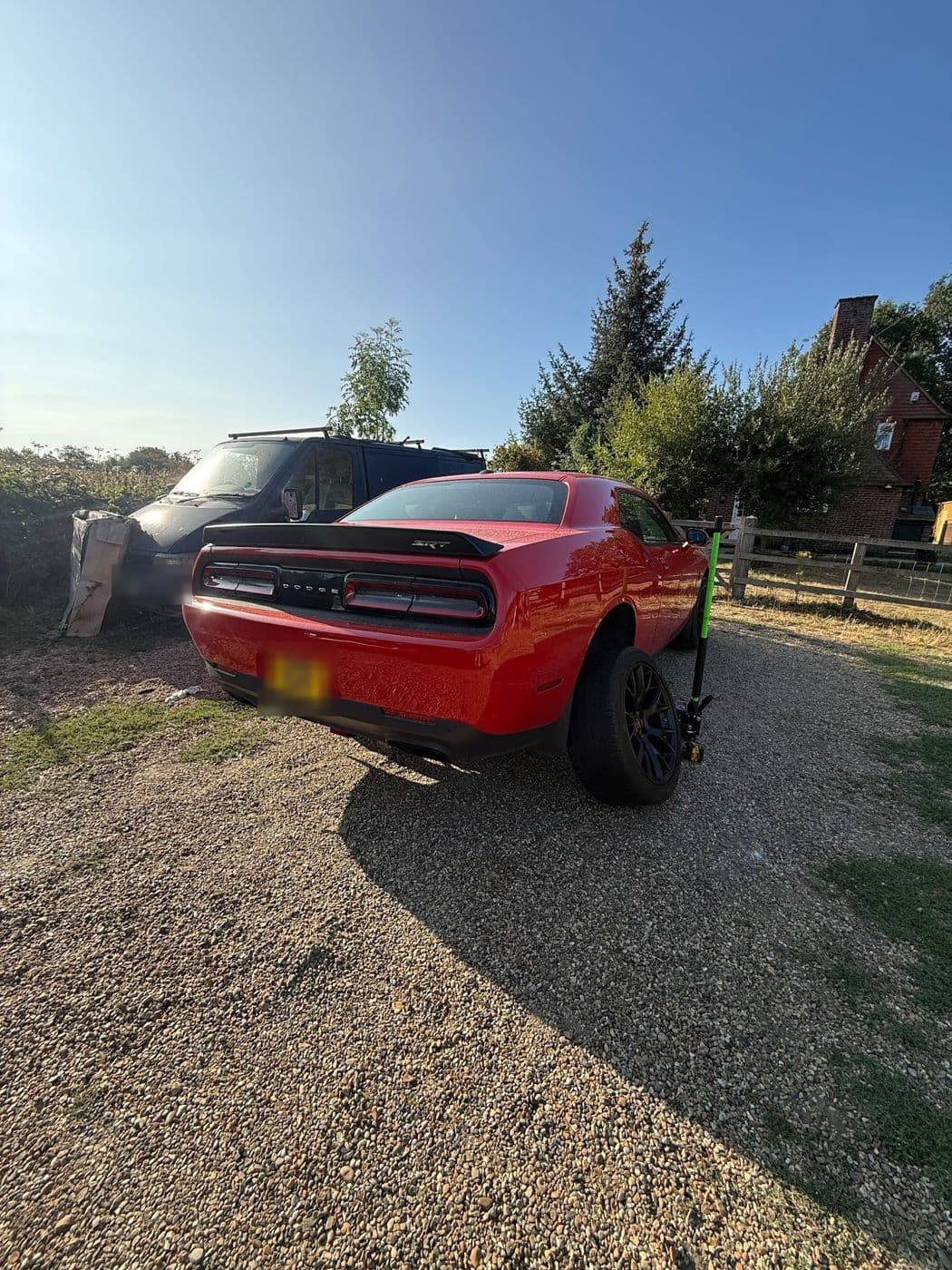 A red Dodge Challenger on a gravel drive with a trolley jack by the rear wheel