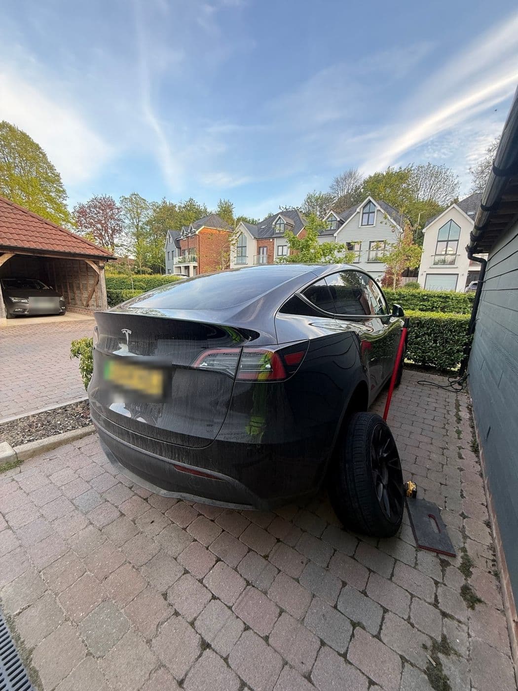A grey Tesla Model Y on a block-paved drive with a rear wheel off and a jack beside it