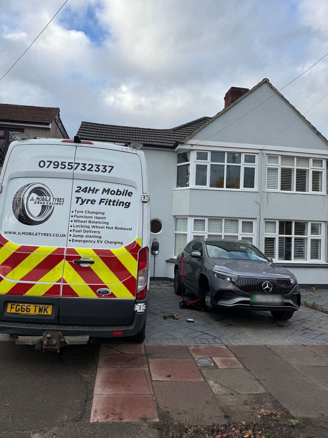 The back of a JL Mobile Tyres van with red and yellow chevrons outside a house, a grey Mercedes on a jack on the drive