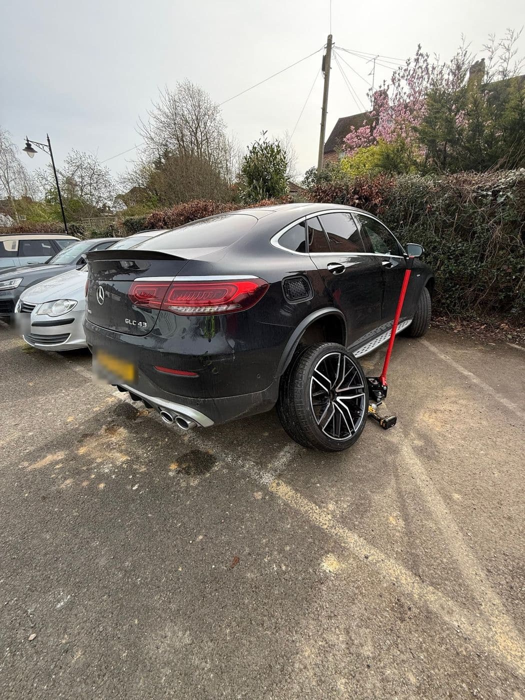 A black Mercedes GLC coupé in a car park with a trolley jack under the rear wheel
